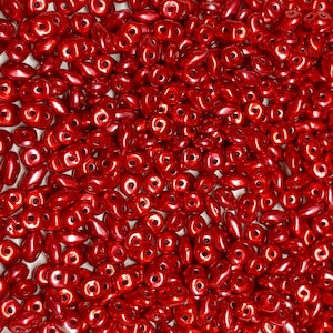May include: A large quantity of small, red, glass beads in a teardrop shape. The beads have a shiny, metallic finish.