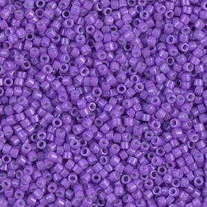 May include: Close-up of a pile of small, cylindrical purple beads. The beads are uniform in size and shape, with a hole running through the center of each. The beads have a glossy finish and are scattered randomly.