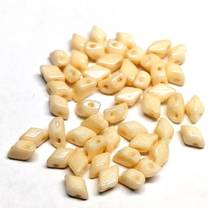 May include: A pile of off-white, faceted glass beads. The beads are shaped like diamonds and have a hole in the center.
