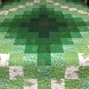 以下が含まれることがあります： 中央にダイヤモンド模様の入った緑と白のパッチワークキルト。キルトは、花柄や幾何学模様など、さまざまなパターンでさまざまな緑色の生地で作られています。
