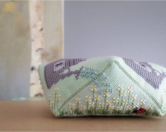 May include: A green and gray fabric pillow with a floral design and a ladybug. The pillow is filled with beads and has a square shape.