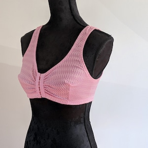 Könnte beinhalten: Ein hellrosa, leicht strukturierter BH mit Frontverschluss auf einer schwarzen Schaufensterpuppe.