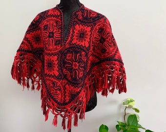 May include: Red and black patterned poncho with fringe trim. The poncho is made of a soft, woven fabric and has a geometric design.