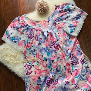 May include: A white nightgown with a floral print in shades of pink, blue, and purple. The nightgown has a lace trim around the neckline and sleeves.