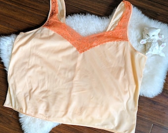 Pode incluir: Uma blusa sem mangas cor pêssego com uma borda de renda em uma cor laranja brilhante.