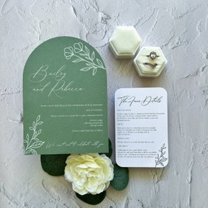May include: A green and white wedding invitation with a floral design. The invitation includes the names "Bailey and Rebecca" and the date "14th of February". The invitation also includes the details of the wedding ceremony and reception.