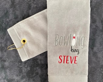 May include: A light gray bowling towel with the words "Bowling king STEVE" embroidered in gray, black, and red. The towel has a white bowling pin graphic and a gold-colored hook.