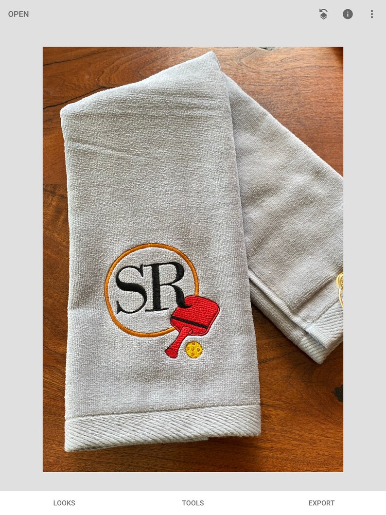 May include: A grey towel with a personalised embroidery design featuring the initials "SR" in a circle with a red and yellow paddle and ball.