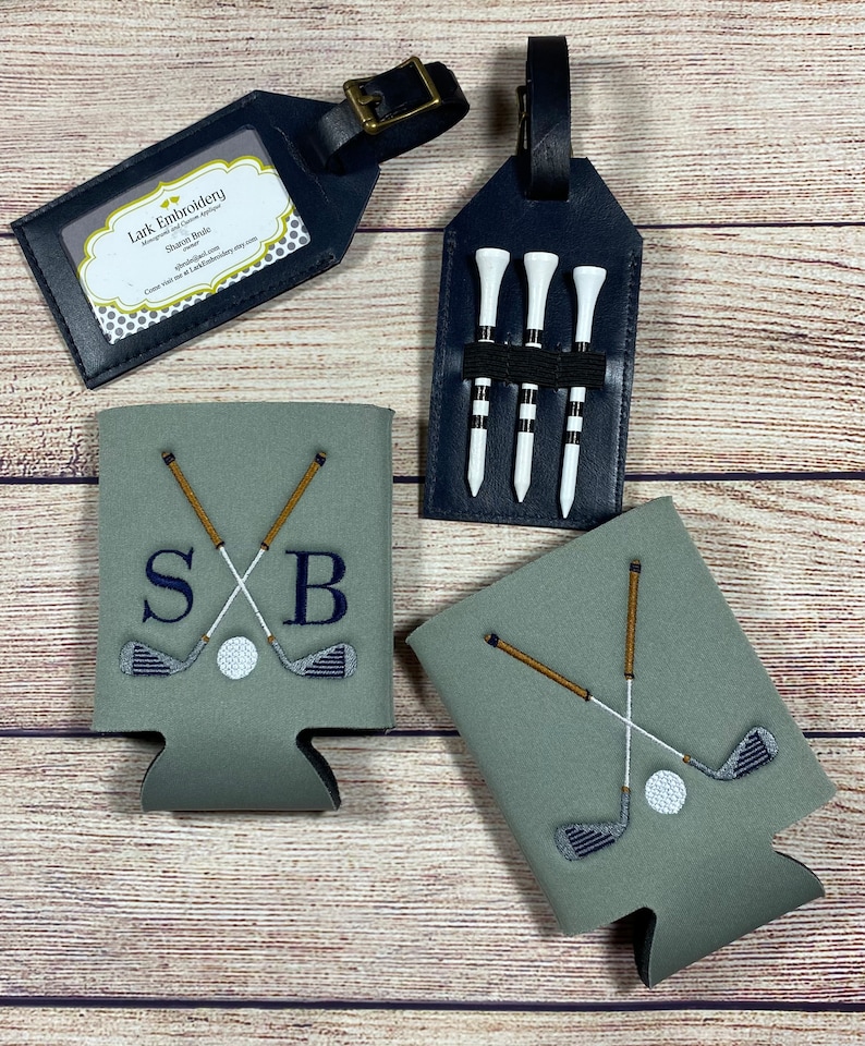 Op de afbeelding: Twee groene en grijze koelers voor blikjes met een golfclub- en balontwerp. Een koeler heeft de initialen "SB" geborduurd. Een zwart leren bagagelabel met vier golftees. Een zwart leren bagagelabel met de tekst "Lark Embroidery" en "Stacey Boyle" erop.