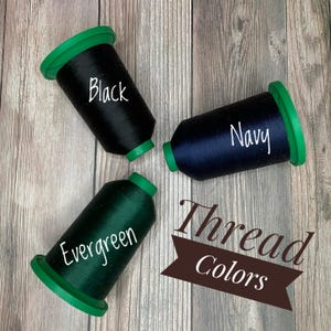 May include: Three spools of thread in black, navy blue, and evergreen green. The spools are labelled with their respective colours. The text "Thread Colours" is written in a brown banner.