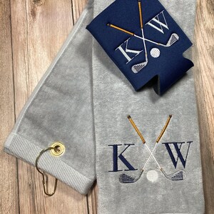 May include: Grey golf towel with a gold ring and a navy blue cooler with a white golf ball and crossed golf clubs embroidered with the letters "KW".