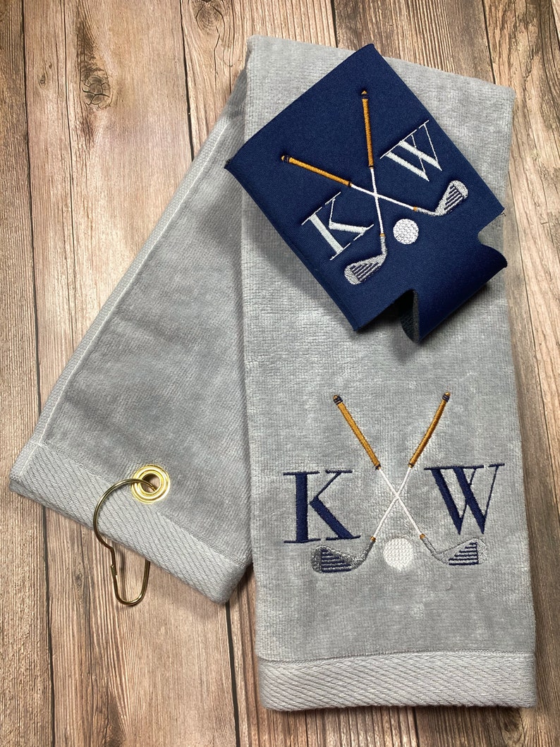 May include: Grey golf towel with a gold ring and a navy blue cooler with a white golf ball and crossed golf clubs embroidered with the letters "KW".