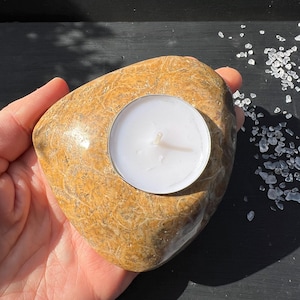 Peut inclure: Un photophore en pierre naturelle avec une bougie chauffe-plat. La pierre est de couleur marron clair avec une surface texturée. La bougie blanche est dans un support métallique.