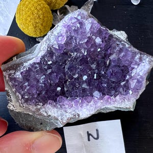Könnte beinhalten: Ein großer Amethyst-Kristall-Cluster in violetter und weißer Farbe. Der Kristall ist roh und hat eine natürliche, raue Textur.