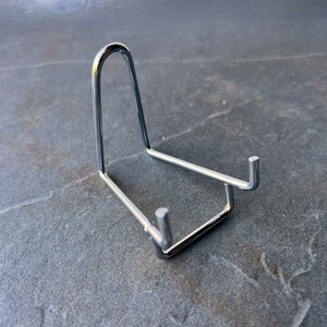 Puede incluir: Un soporte de exhibici&oacute;n de metal plateado para un objeto peque&ntilde;o, como una roca o un cristal.