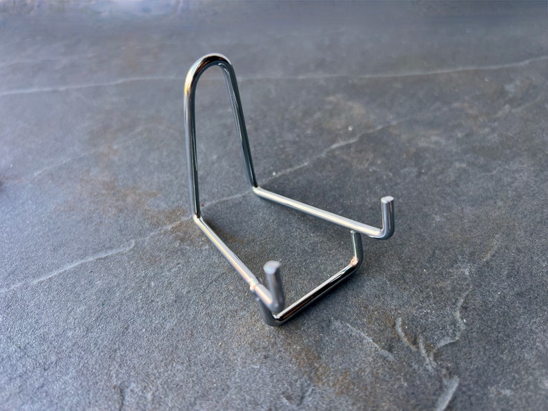 Puede incluir: Un soporte de exhibici&oacute;n de metal plateado para un objeto peque&ntilde;o, como una roca o un cristal.