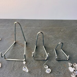 Puede incluir: Tres soportes de exhibici&oacute;n de metal plateado de diferentes tama&ntilde;os. Los soportes tienen forma triangular y un acabado liso y pulido.