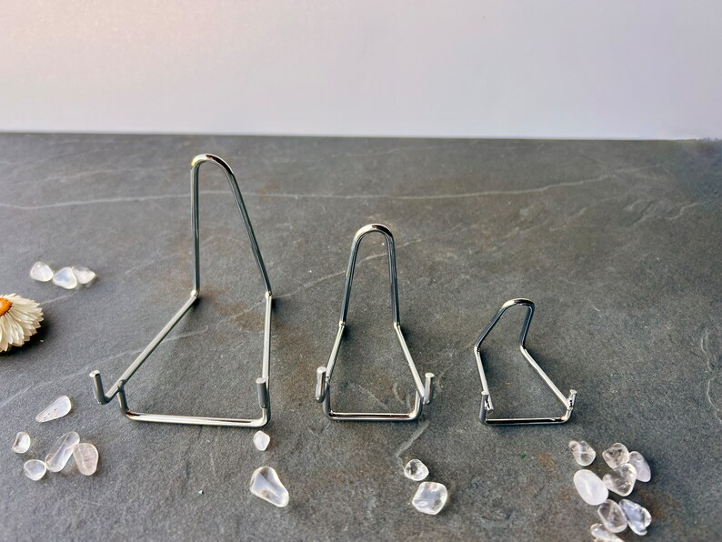 Puede incluir: Tres soportes de exhibici&oacute;n de metal plateado de diferentes tama&ntilde;os. Los soportes tienen forma triangular y un acabado liso y pulido.