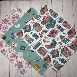 Puede incluir: Cuatro pa&ntilde;os cuadrados de tela con diferentes estampados. Uno tiene flores rosas, otro tiene libros y tazas de t&eacute;, y el tercero tiene libros envueltos como regalos. El cuarto pa&ntilde;o tiene un estampado de libros.