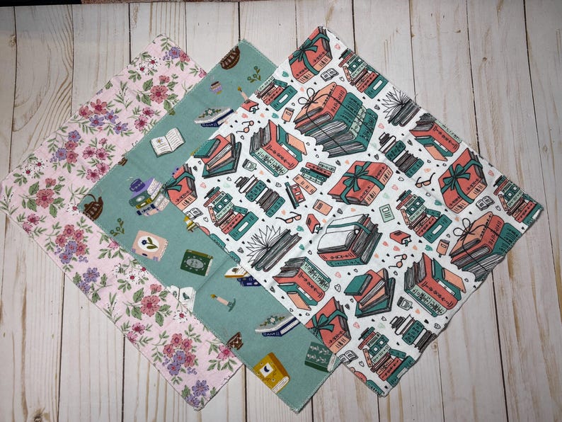 Puede incluir: Cuatro pa&ntilde;os cuadrados de tela con diferentes estampados. Uno tiene flores rosas, otro tiene libros y tazas de t&eacute;, y el tercero tiene libros envueltos como regalos. El cuarto pa&ntilde;o tiene un estampado de libros.
