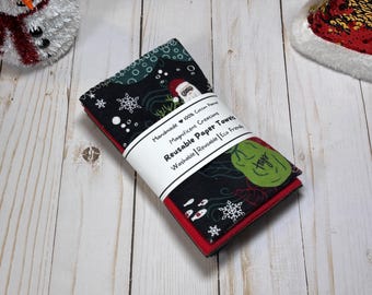 May include: A stack of reusable paper towels with a festive Christmas theme. The towels are black with red trim and feature snowflakes, Santa, and other holiday designs. The label reads "Reusable Paper Towels".