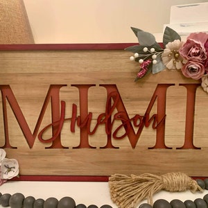 Pu&ograve; includere: Cartello in legno con i nomi "MIMI" e "Hudson" intagliati in rosso. Il cartello &egrave; decorato con fiori artificiali e un nappa di iuta. Il cartello ha un bordo rosso e uno sfondo in legno.