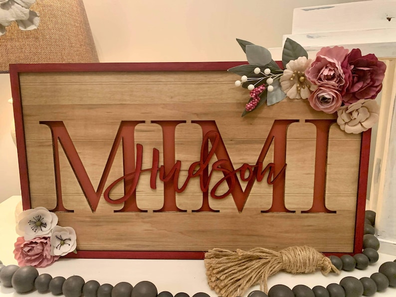 Pu&ograve; includere: Cartello in legno con i nomi "MIMI" e "Hudson" intagliati in rosso. Il cartello &egrave; decorato con fiori artificiali e un nappa di iuta. Il cartello ha un bordo rosso e uno sfondo in legno.