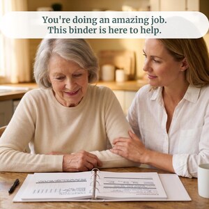 May include: A white three-ring binder lies open on a wooden table, displaying printed pages with charts and text. The text at the top of the image reads, "You're doing an amazing job. This binder is here to help." Two white ceramic mugs are present.