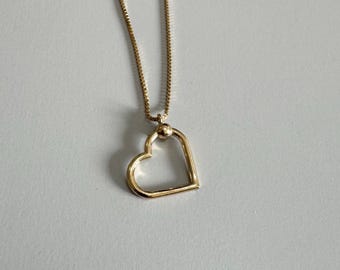 May include: A gold chain necklace with a heart-shaped pendant. The pendant is open and has a small ball at the top.