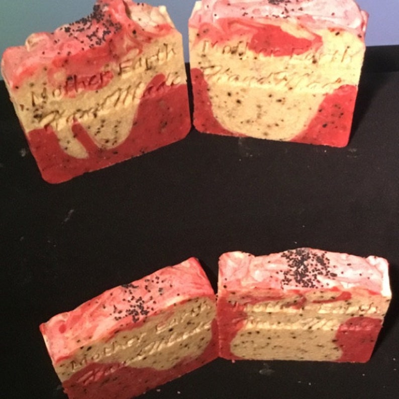 Puede incluir: Cuatro barras de jab&oacute;n hecho a mano con un dise&ntilde;o de remolino rojo y blanco. El jab&oacute;n est&aacute; decorado con semillas de amapola negras y tiene el texto "Mother Earth Handmade" en las barras.