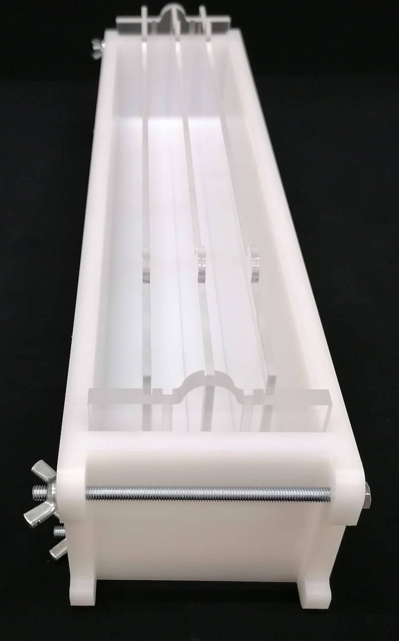 Puede incluir: Molde de pl&aacute;stico blanco con un inserto de acr&iacute;lico transparente. El molde tiene una forma rectangular larga y se mantiene unido por una varilla de metal con tuercas de mariposa. El inserto de acr&iacute;lico tiene cuatro ranuras verticales y un fondo curvo.