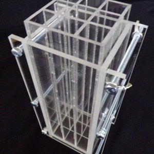 Può includere: Uno stampo in acrilico trasparente con un motivo a griglia, tenuto insieme da viti metalliche. Lo stampo è progettato per creare più oggetti piccoli.