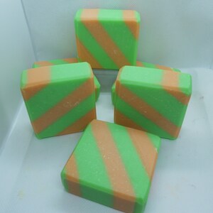 Puede incluir: Cinco barras de jab&oacute;n rayadas de verde y naranja en una caja blanca. Las barras de jab&oacute;n est&aacute;n dispuestas en forma de pir&aacute;mide.