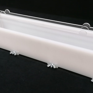 Puede incluir: Un molde de jab&oacute;n rectangular blanco con una tapa de acr&iacute;lico transparente. El molde tiene abrazaderas met&aacute;licas en los lados para asegurar la tapa.