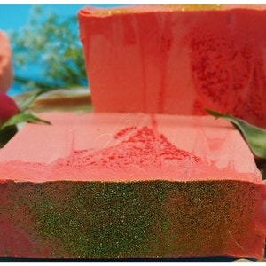 Puede incluir: Dos barras de jab&oacute;n hechas a mano con una base roja y purpurina verde en la parte superior. El jab&oacute;n tiene forma rectangular.