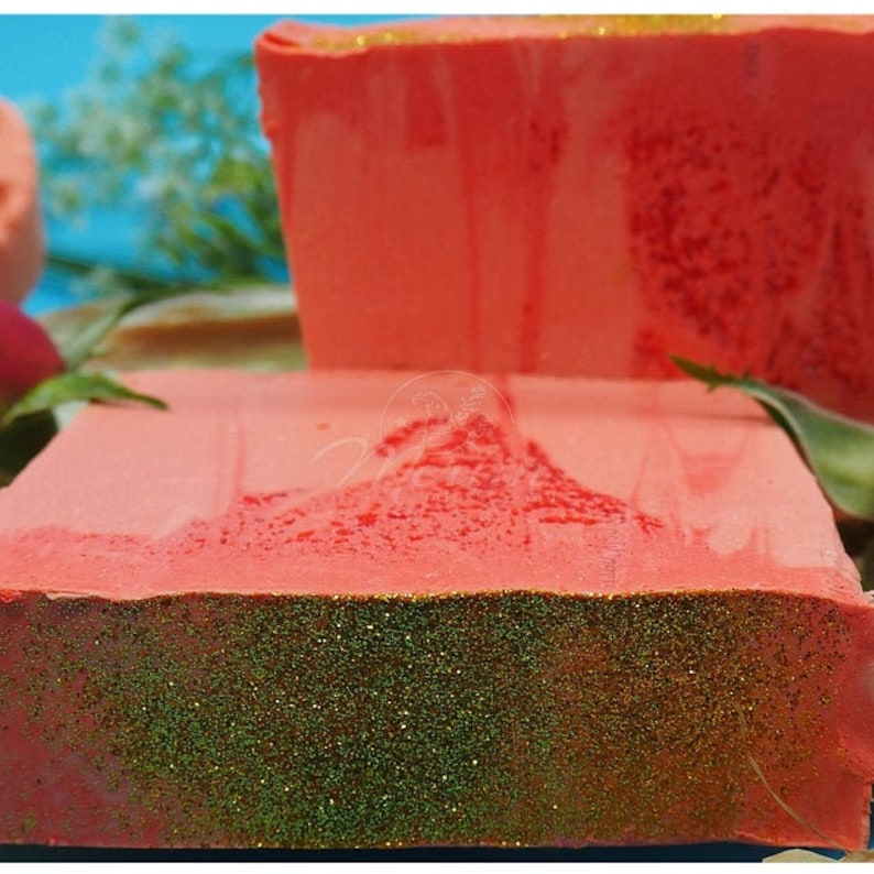 Puede incluir: Dos barras de jab&oacute;n hechas a mano con una base roja y purpurina verde en la parte superior. El jab&oacute;n tiene forma rectangular.