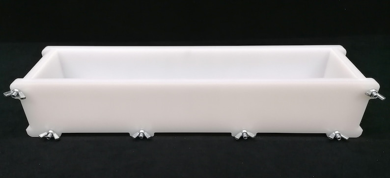 Puede incluir: Molde de jab&oacute;n rectangular blanco con soportes de esquina de metal. El molde est&aacute; hecho de pl&aacute;stico y tiene una superficie lisa.