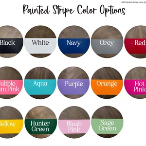 May include: A color chart displaying painted stripe color options. Each color is presented on a circular wooden background with a horizontal stripe of color across the center. Colors include black, white, navy, grey, red, bubble gum pink, aqua, purple, orange, hot pink, yellow, hunter green, blush pink, and sage green.