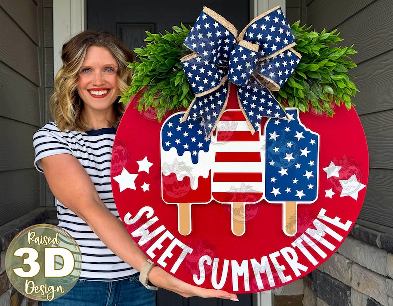 Op de afbeelding: Een rond rood houten deurbord met drie ijsjesafbeeldingen in Amerikaanse vlagpatronen, groen kunstblad en een grote blauw-witte strik van jute met sterrenpatroon. De tekst SWEET SUMMERTIME staat in witte letters aan de onderkant.