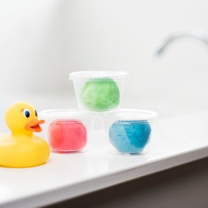 May include: Three clear plastic containers with lids, each containing a different colored play dough. The colors are green, pink, and blue. A yellow rubber duck is in the foreground.