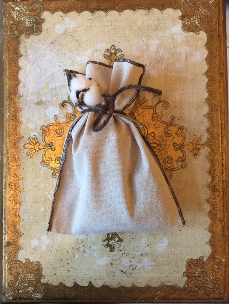 May include: A small, off-white fabric pouch with a brown drawstring closure. The pouch is tied with a brown cord and has a small bunch of white cotton on top.