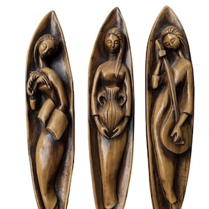May include: Three wooden wall sculptures of women in flowing robes. One holds a book, another a vase, and the third plays a stringed instrument. Each figure is set within a leaf-shaped frame, all in a warm brown colour.
