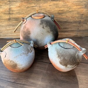 May include: Three ceramic jars with lids, each with a unique glaze pattern. The jars are tied with natural twine and have a rustic, handmade look.