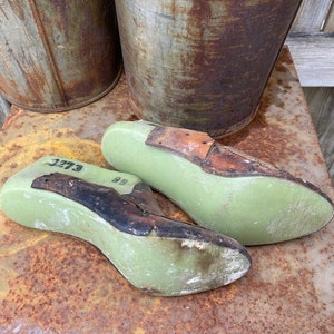 May include: Two green shoe lasts with brown leather straps. The lasts are marked with the numbers "3273" and "99".