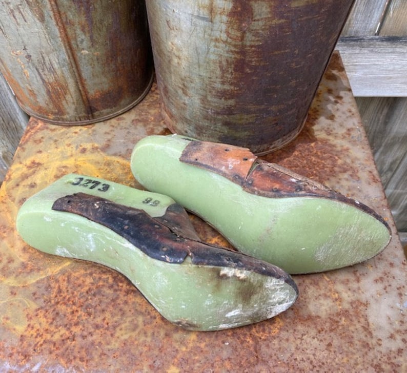 May include: Two green shoe lasts with brown leather straps. The lasts are marked with the numbers "3273" and "99".