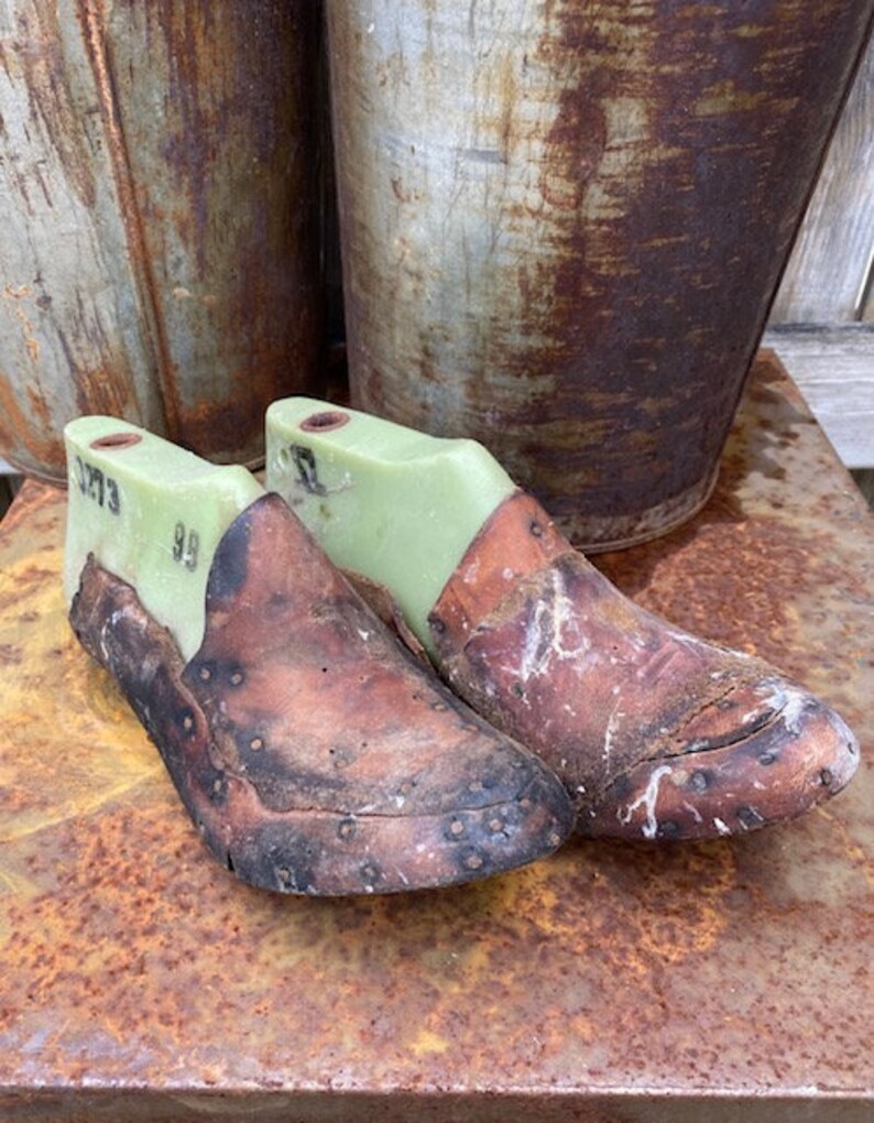 May include: Two brown leather shoe lasts with green plastic bases. The lasts are worn and have a rough texture. The numbers "373" and "99" are visible on the lasts.