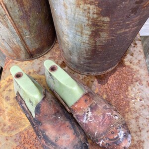 May include: Two brown leather shoe forms with green plastic inserts. The shoe forms are sitting on a rusty metal surface.