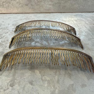 Könnte beinhalten: Drei antike Kamin-Fender-Abschnitte aus Messing. Jeder Abschnitt hat eine gebogene, bogenförmige Form mit einer Reihe von vertikalen, wellenförmigen, dekorativen Elementen. Das Messing hat eine warme, gealterte Patina, die auf Vintage-Handwerkskunst hindeutet. Die Abschnitte sind auf einer grauen Oberfläche angeordnet.