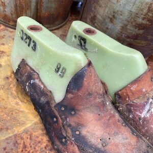 May include: Two vintage shoe lasts made of green plastic with leather coverings. The lasts are numbered "3273" and "32".