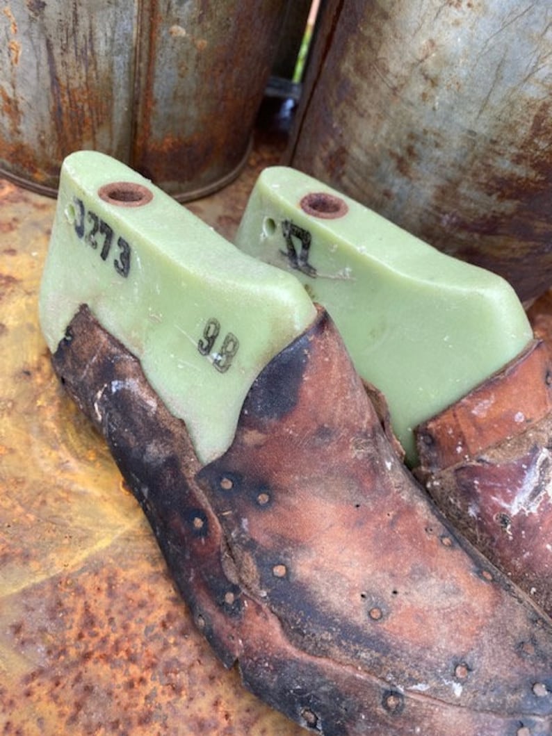May include: Two vintage shoe lasts made of green plastic with leather coverings. The lasts are numbered "3273" and "32".